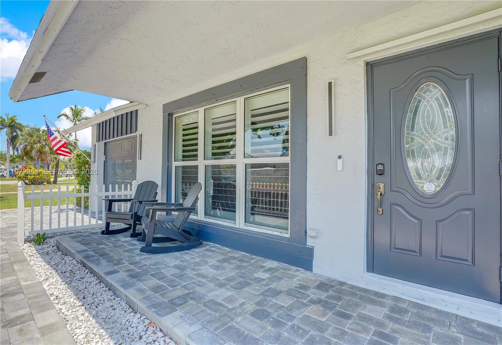 A gray front door and two rocking chairs sit on a paved porch — 1315 Gallinule Dr, Delray Beach FL 33444, DELRAY BEACH, FL