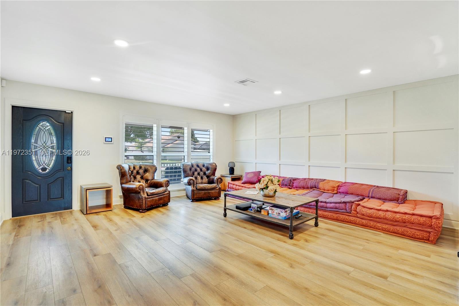 A living room features light wood flooring, a paneled wall, and a low-profile modular sofa — 1315 Gallinule Dr, Delray Beach FL 33444, DELRAY BEACH, FL