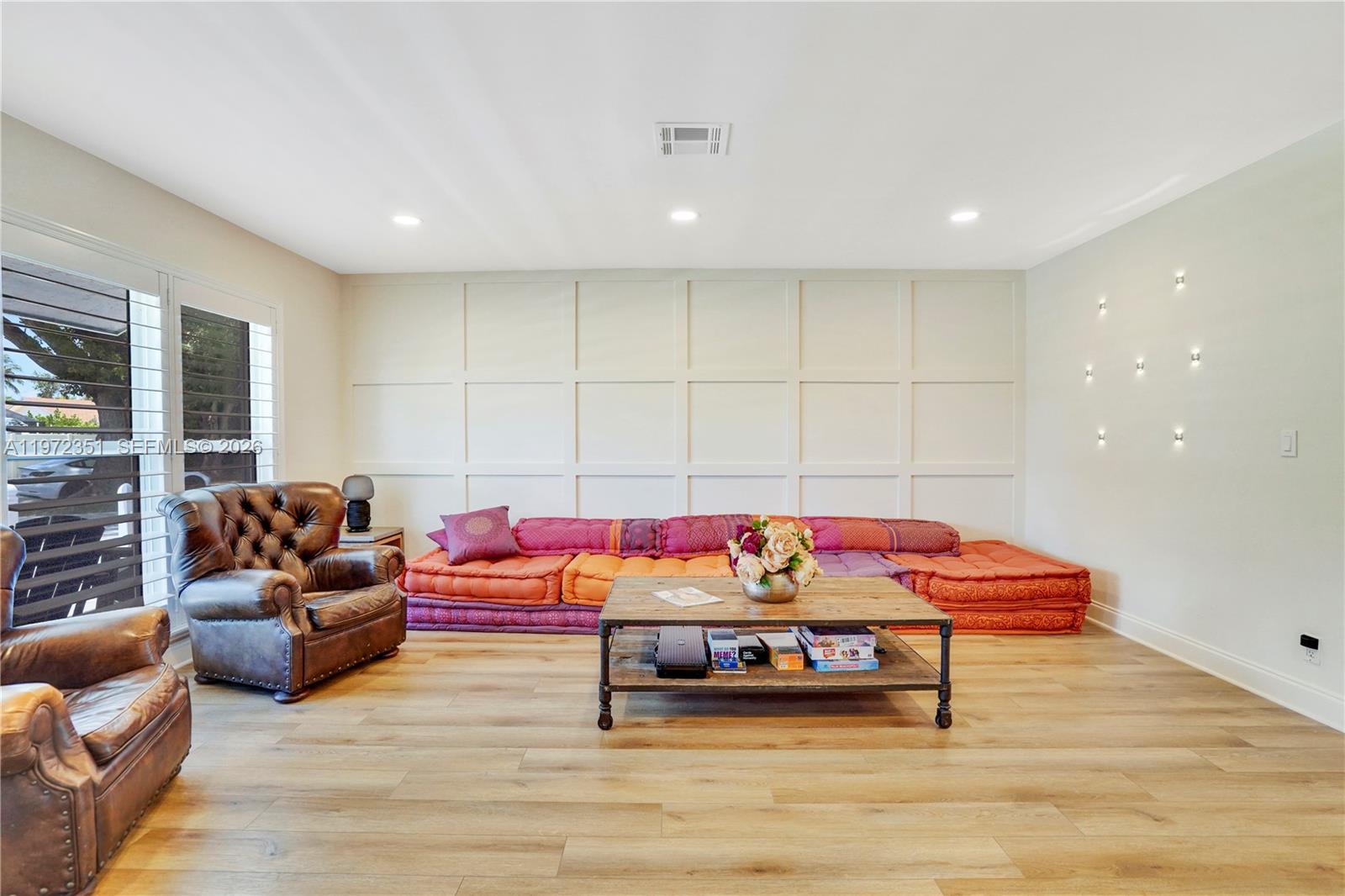 A living room features a low, colorful floor sofa, a wooden coffee table, and wainscoting — 1315 Gallinule Dr, Delray Beach FL 33444, DELRAY BEACH, FL