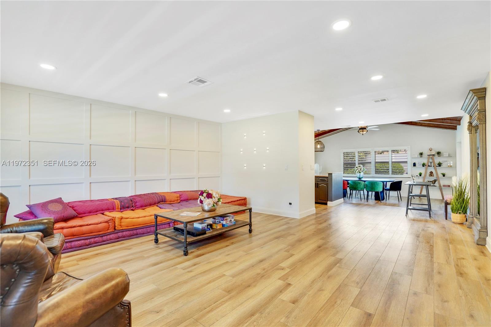 A living room features a low-profile colorful sofa, wood flooring, and a paneled accent wall — 1315 Gallinule Dr, Delray Beach FL 33444, DELRAY BEACH, FL