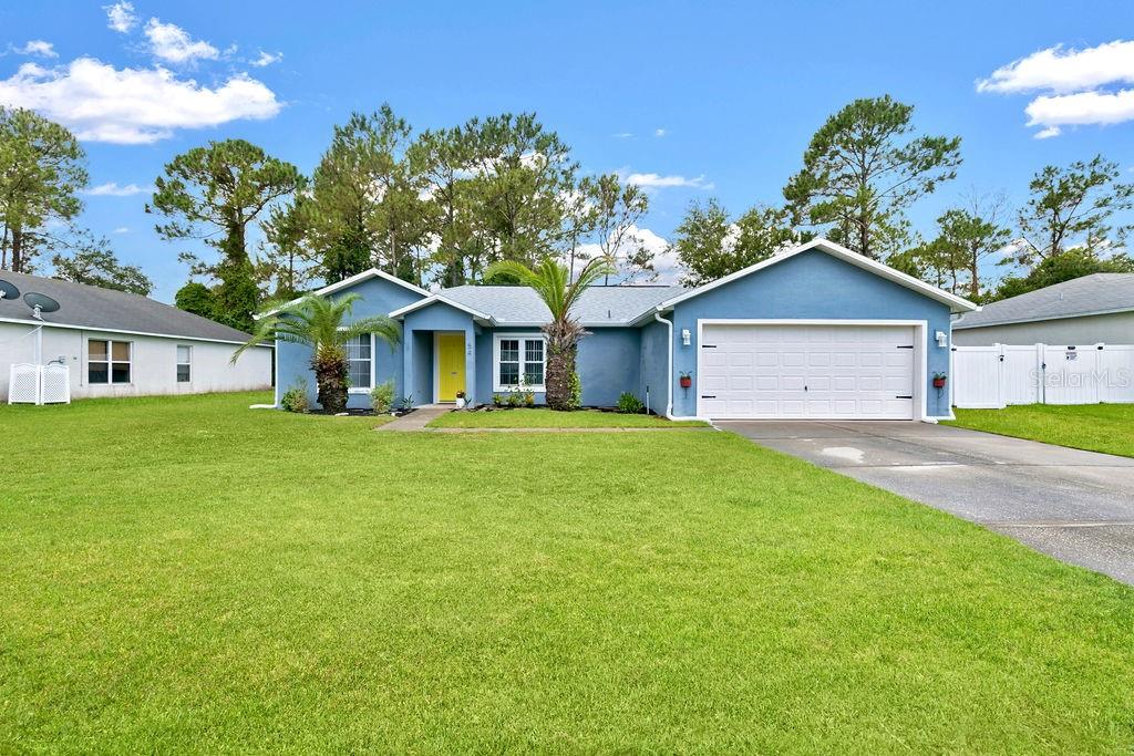A blue single-story house with a white garage door and a bright yellow front door — 54 PENNSYLVANIA LANE, PALM COAST, FL