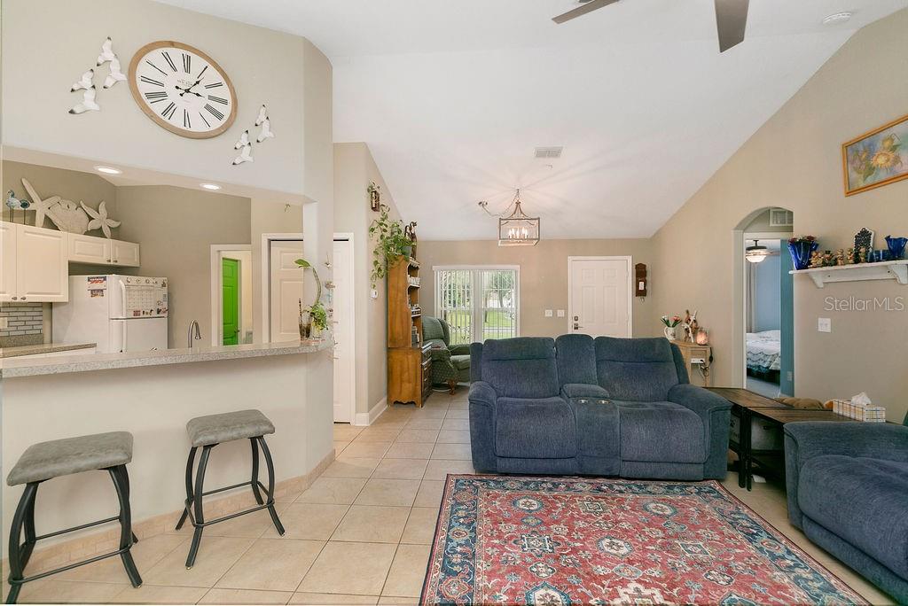 A living room with tile floors, a blue sofa, and an open kitchen with bar seating — 54 PENNSYLVANIA LANE, PALM COAST, FL