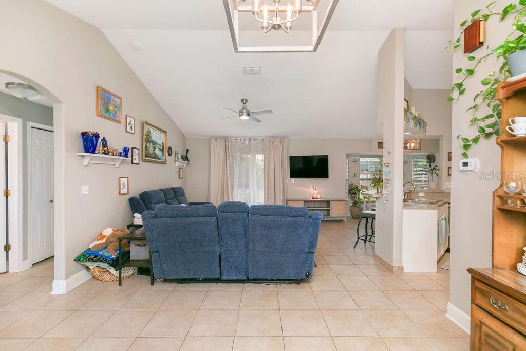 A living room with tile floors, blue reclining sofas, and an open kitchen layout — 54 PENNSYLVANIA LANE, PALM COAST, FL
