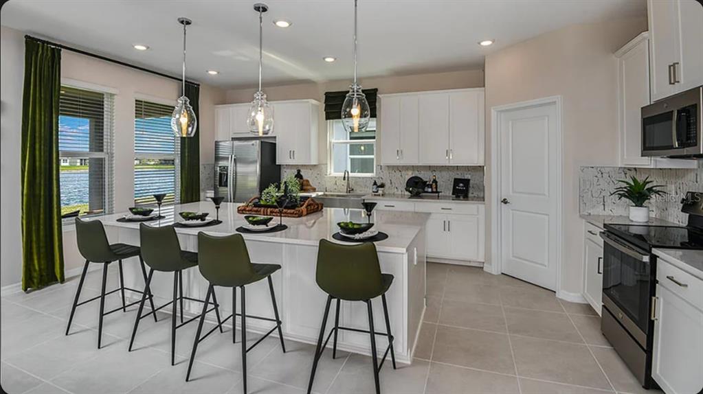 A modern kitchen features white cabinets, a large quartz island with four stools, and pendant lighting — 5392 GUNWALE DRIVE, COCOA, FL