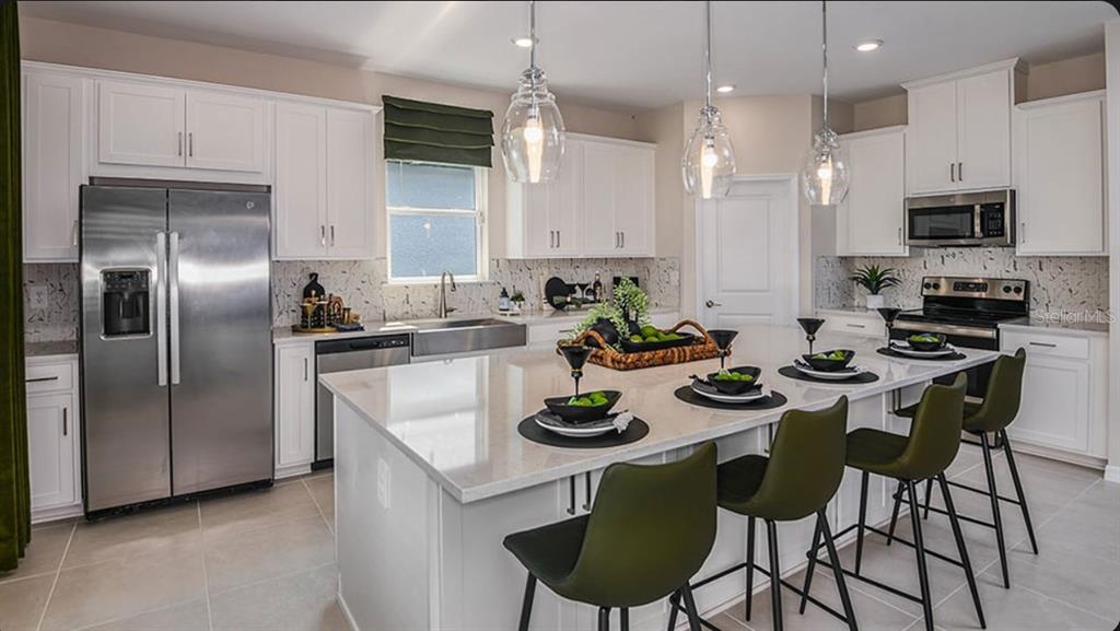 A kitchen with white cabinets, stainless steel appliances, a large island, and olive green chairs — 5392 GUNWALE DRIVE, COCOA, FL