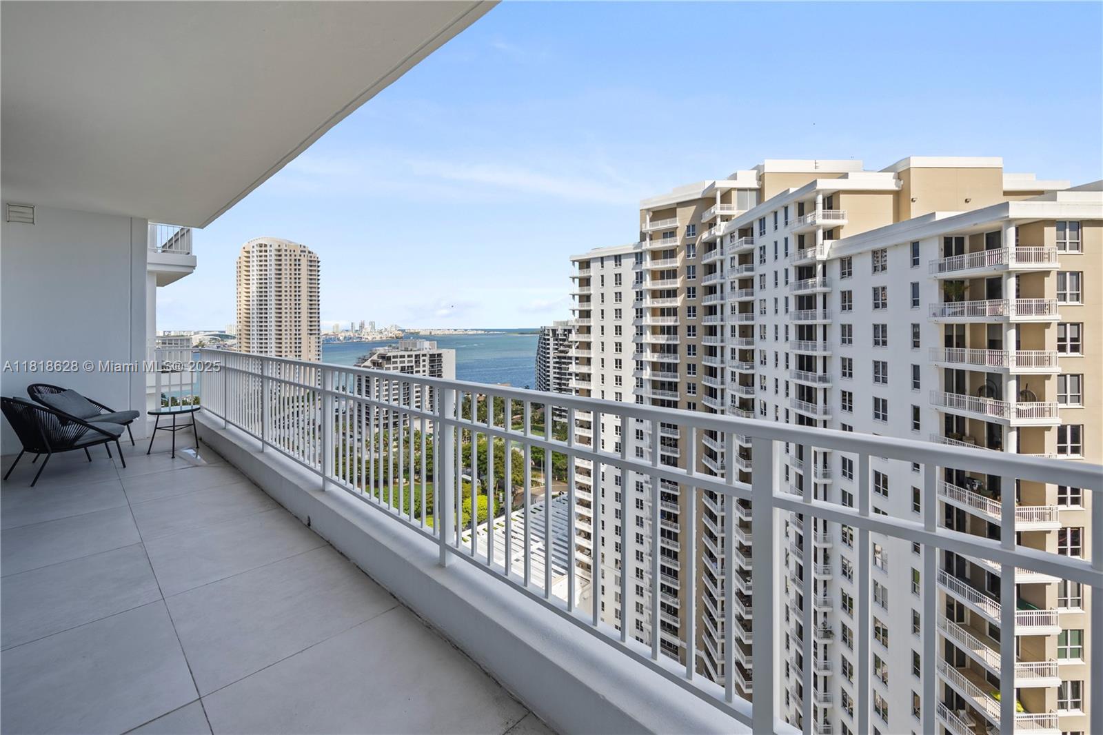 A balcony with tile flooring and a white railing overlooks a bay and high-rise buildings — 801 Brickell Key Blvd # 2203, Miami FL 33131, MIAMI, FL