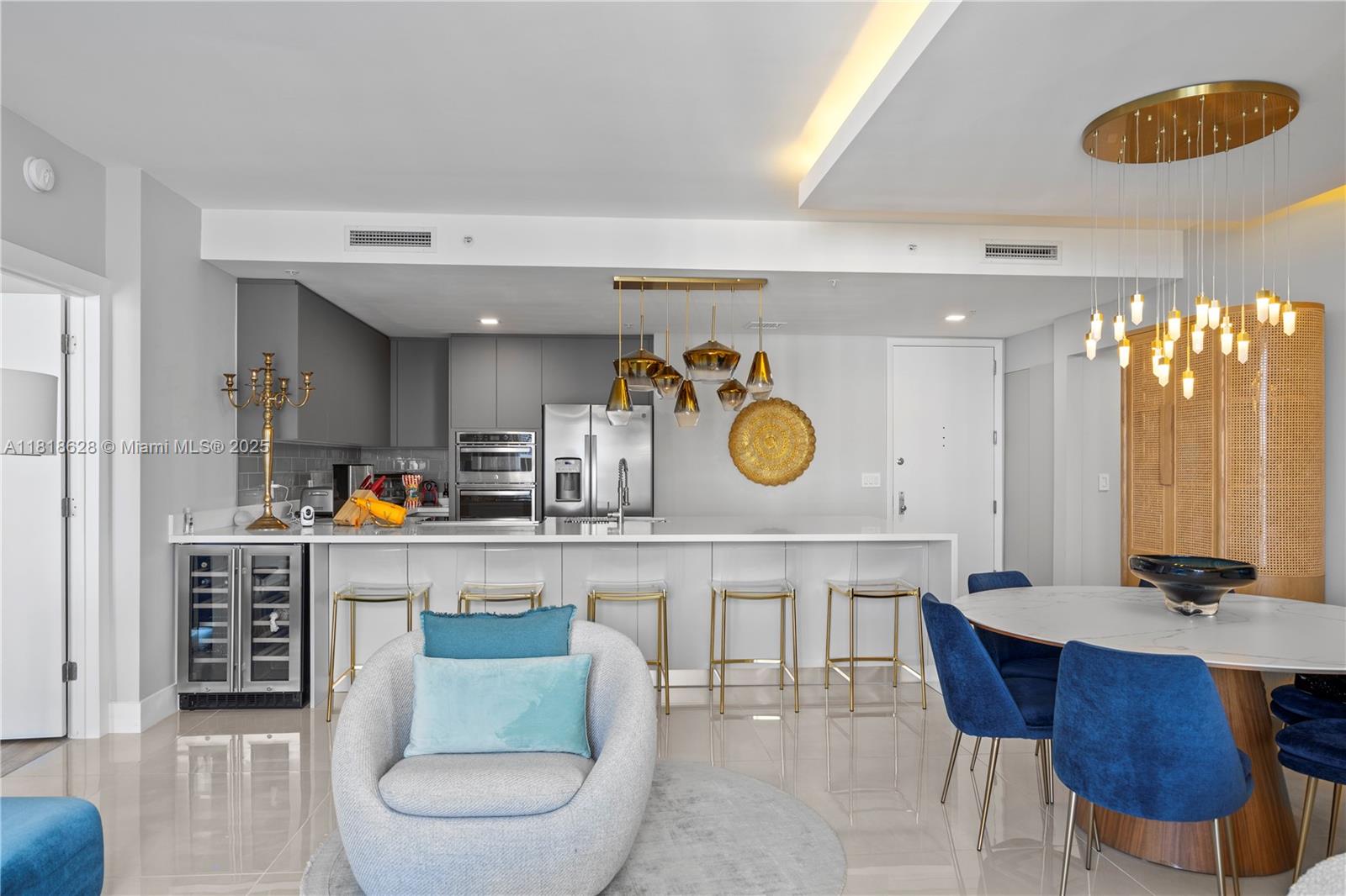 A modern kitchen features white countertops, gold bar stools, and a dining area with blue chairs — 801 Brickell Key Blvd # 2203, Miami FL 33131, MIAMI, FL