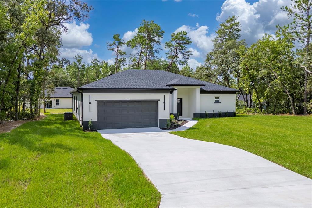 A modern single-story house with a white exterior, dark gray roof, and a concrete driveway — 455 MARION OAKS PASS, OCALA, FL