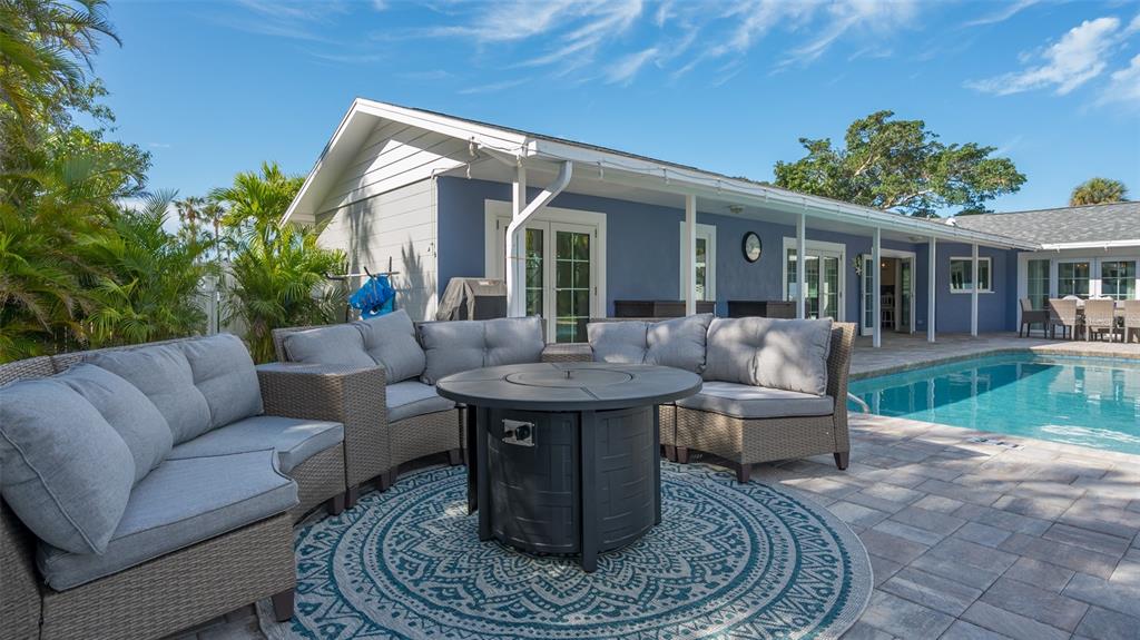 A patio with a sectional sofa, fire pit, and rug overlooks a backyard swimming pool — 500 SCHOONER LANE, LONGBOAT KEY, FL