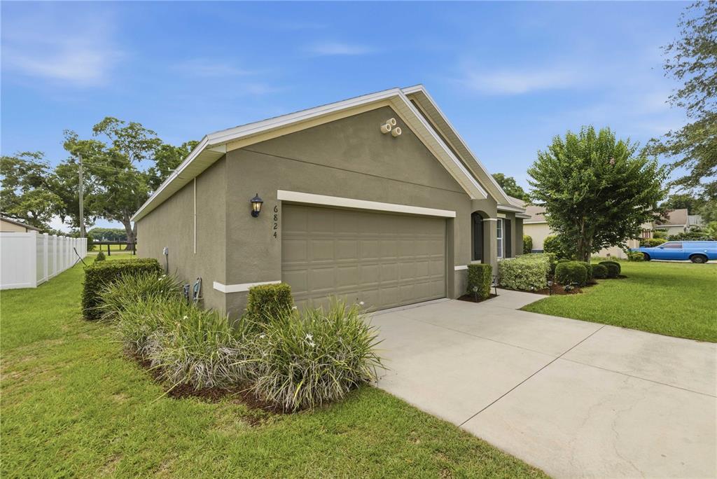 A single-story house with a tan stucco exterior, a two-car garage, and a concrete driveway — 6824 SW 64TH TERRACE, OCALA, FL