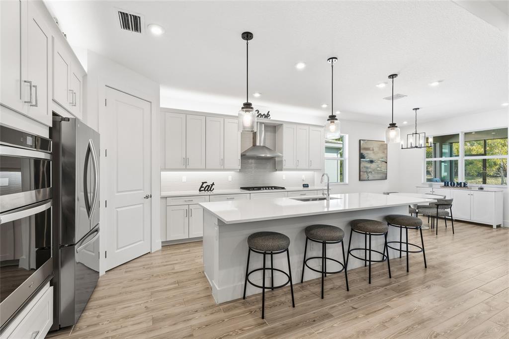 A modern white kitchen features a large island with bar stools and stainless steel appliances — 11959 SW VIRIDIAN BOULEVARD, PORT ST LUCIE, FL