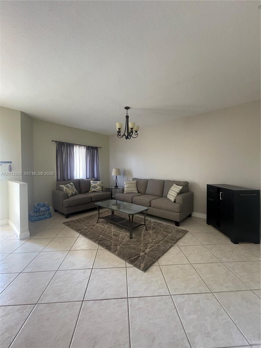 A living room features a gray sofa and loveseat, a glass coffee table, and tile flooring — 10720 NW 66th St # 510, Doral FL 33178, DORAL, FL