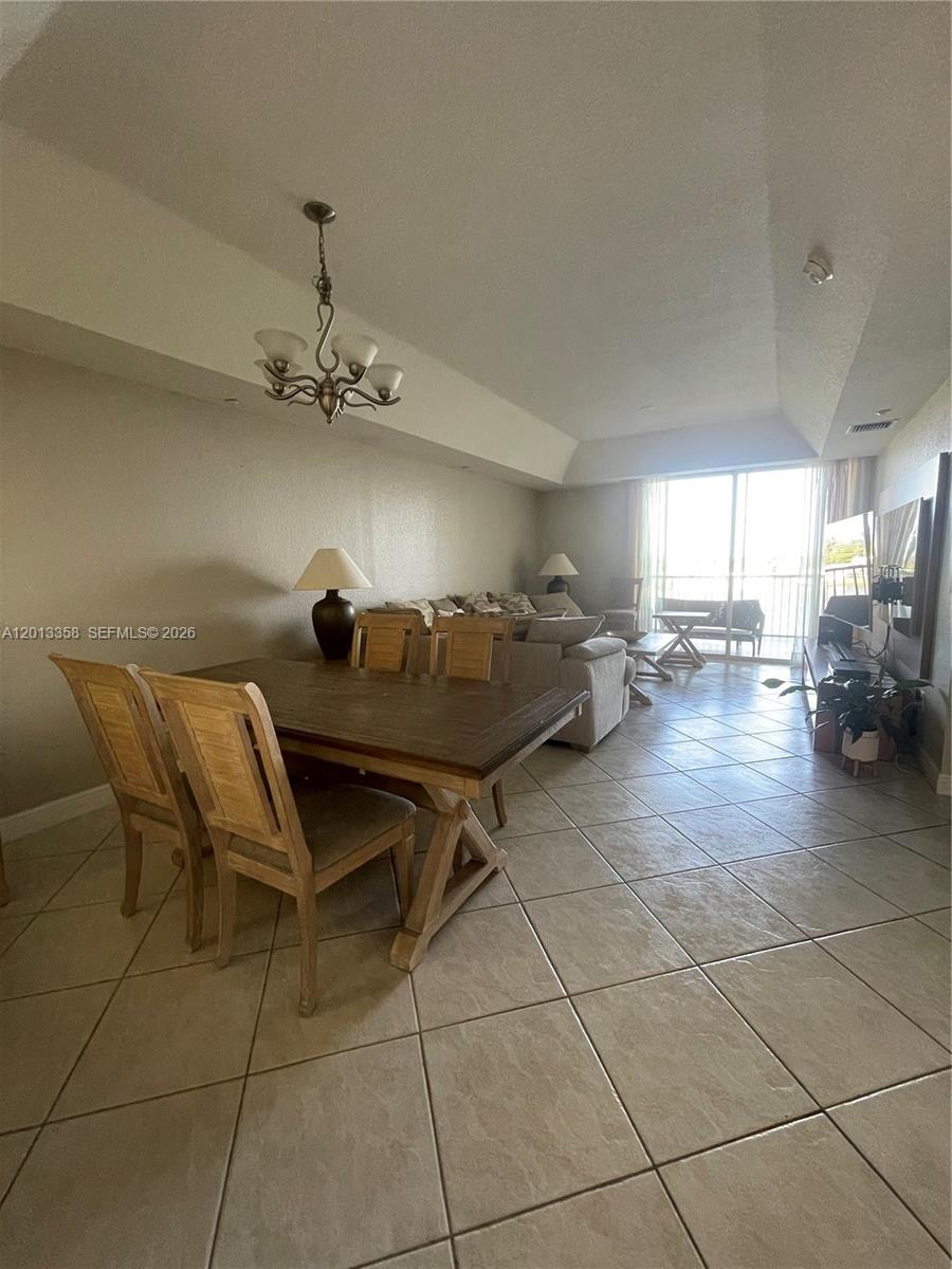 This open-concept living and dining area features tile flooring, a chandelier, and sliding glass doors — 10720 NW 66th St # 510, Doral FL 33178, DORAL, FL