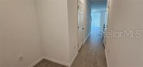 A hallway with light wood-look flooring leads toward a bright room with a glass door — 2126 CRAPE JASMINE LANE, ORLANDO, FL