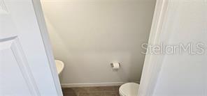 A small bathroom features a white toilet and a toilet paper holder on a plain wall — 2126 CRAPE JASMINE LANE, ORLANDO, FL
