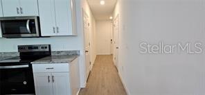 A kitchen with white cabinets and stainless steel appliances leads into a hallway — 2126 CRAPE JASMINE LANE, ORLANDO, FL