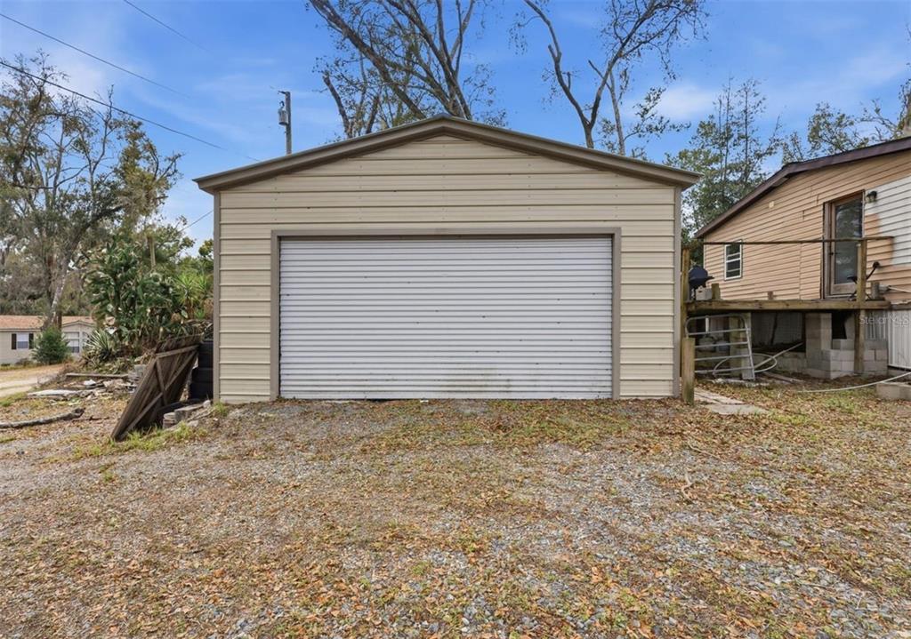 A detached garage with beige horizontal siding and a white roll-up door — 36301 PEAK STREET, ZEPHYRHILLS, FL