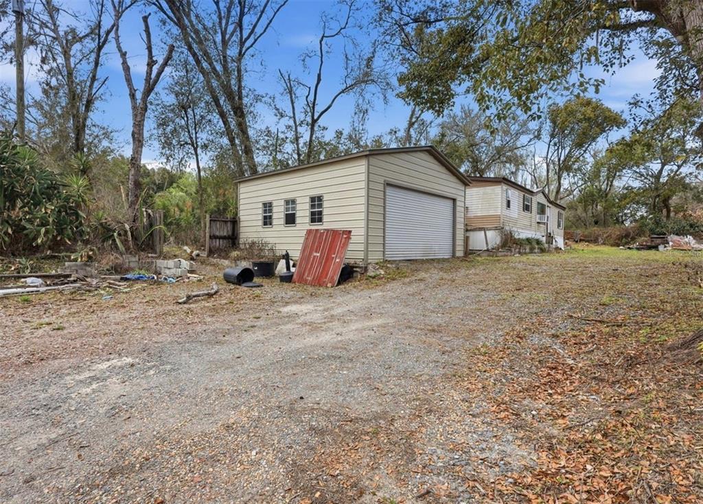 A detached metal garage sits on a gravel lot next to a mobile home — 36301 PEAK STREET, ZEPHYRHILLS, FL