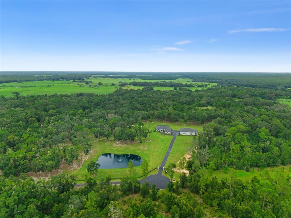 An aerial view shows a house with a pond and driveway surrounded by forest — 1825 W OAK VALLEY COURT, HOMOSASSA, FL
