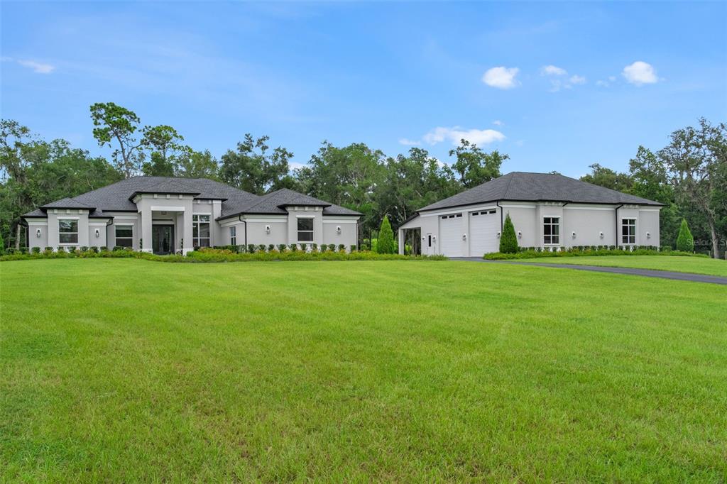 A modern single-story house with a detached garage sits on a large, grassy lawn — 1825 W OAK VALLEY COURT, HOMOSASSA, FL