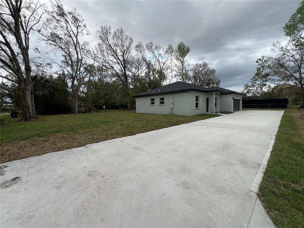 A gray house with a large concrete driveway sits on a grassy lot with trees — 6425 CURTIS STREET, ORLANDO, FL