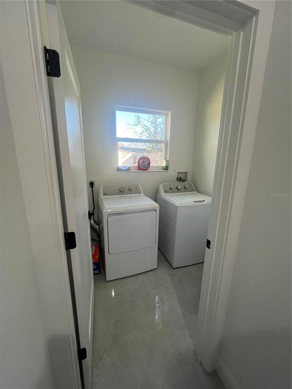 A laundry room features two white appliances, a window, and light-colored tile flooring — 6425 CURTIS STREET, ORLANDO, FL