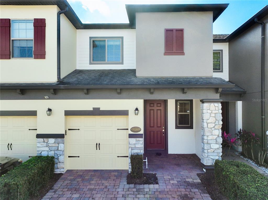 The exterior of a two-story townhouse features a garage, stone accents, and a brick driveway — 2592 ECON LANDING BOULEVARD, ORLANDO, FL