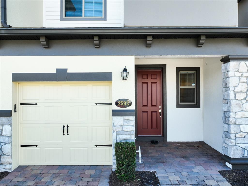 A two-story townhouse exterior features a cream garage door, a red front door, and stone accents — 2592 ECON LANDING BOULEVARD, ORLANDO, FL