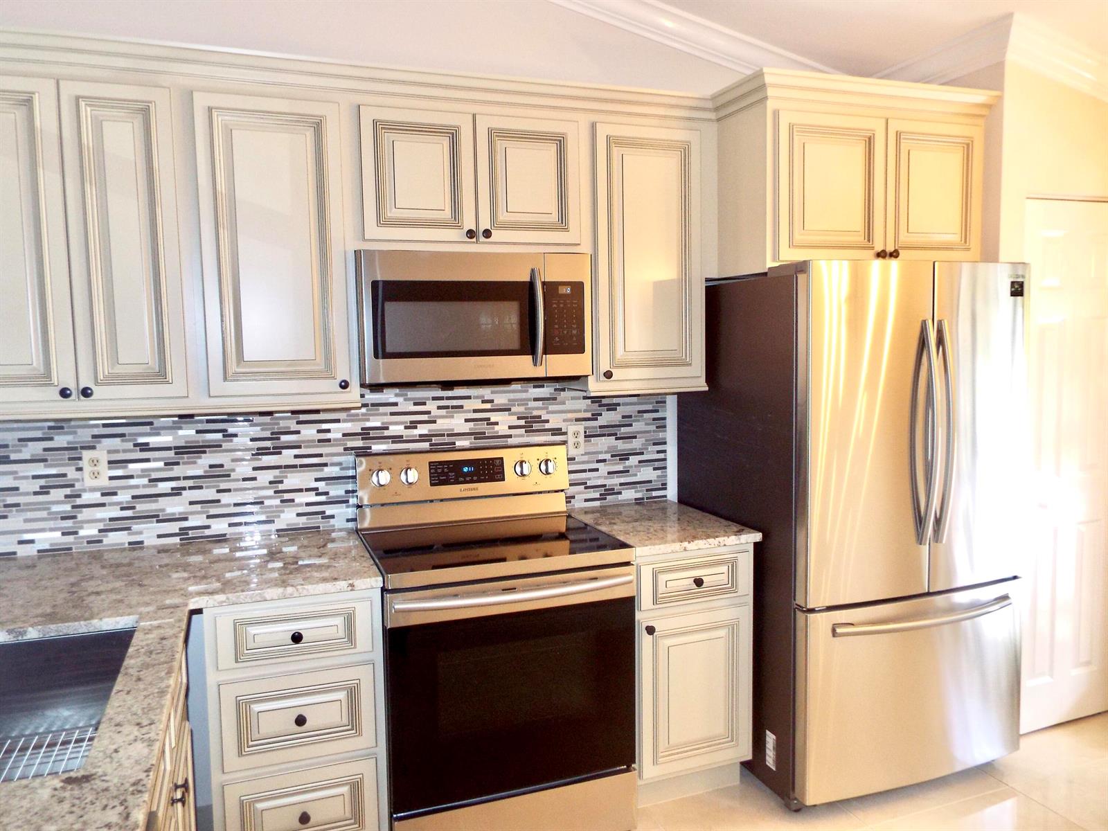 A kitchen featuring cream-colored cabinets, stainless steel appliances, granite countertops, and a mosaic tile backsplash — 3350 Perimeter Drive # 1323, FL 33467, FL