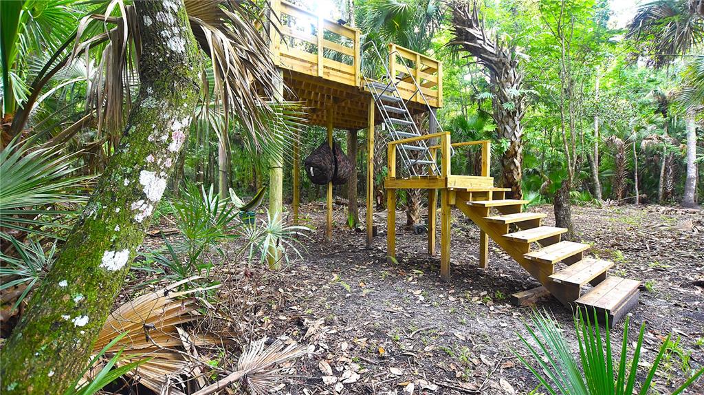 A wooden elevated deck with stairs and a metal ladder stands in a wooded area — VOLCO ROAD, EDGEWATER, FL