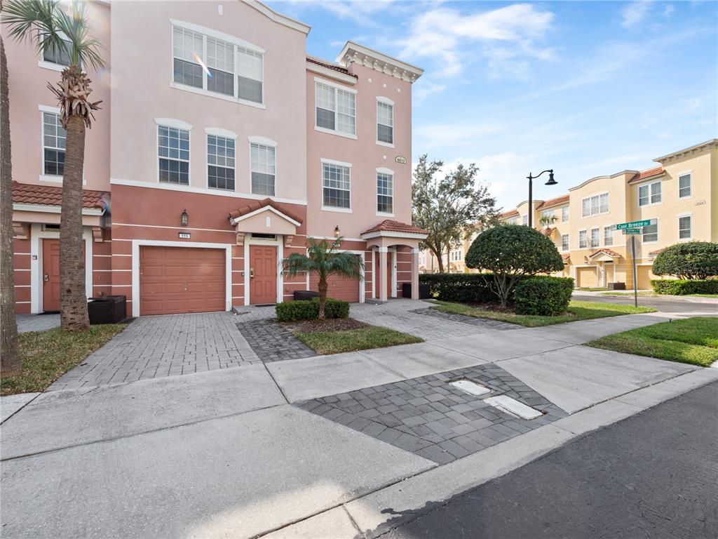 A three-story townhouse with a pink stucco exterior, a garage, and a paved driveway — 8013 COOL BREEZE DRIVE UNIT 116, ORLANDO, FL