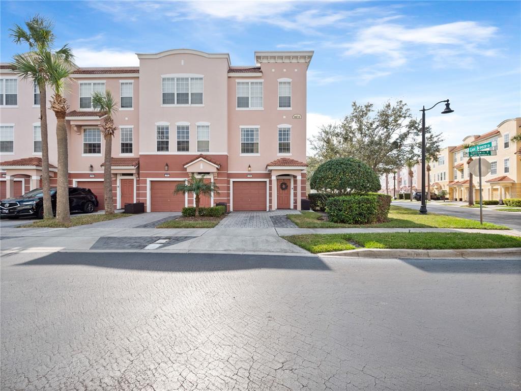 A three-story townhouse with a light pink facade, two garages, and a paved driveway — 8013 COOL BREEZE DRIVE UNIT 116, ORLANDO, FL