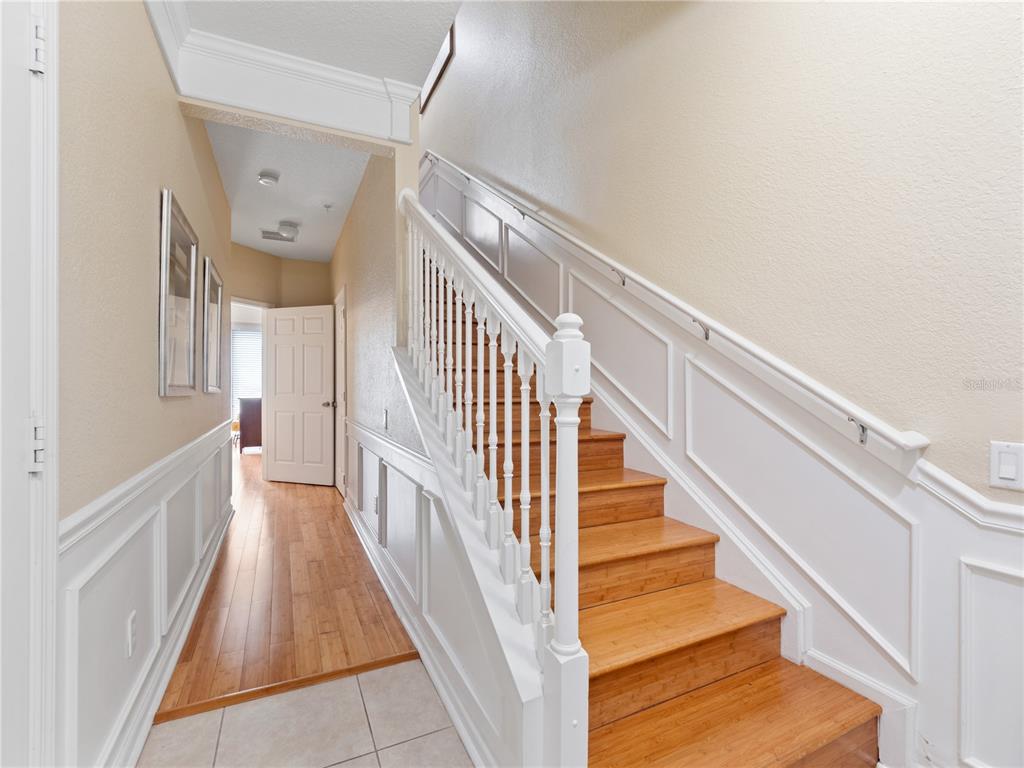 A hallway features a wooden staircase with white railings, wainscoting, and light-colored tile flooring — 8013 COOL BREEZE DRIVE UNIT 116, ORLANDO, FL