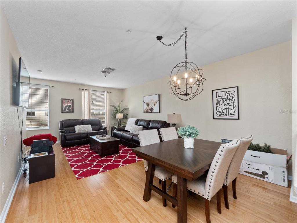 A living and dining area features hardwood floors, a red patterned rug, and a chandelier — 8013 COOL BREEZE DRIVE UNIT 116, ORLANDO, FL