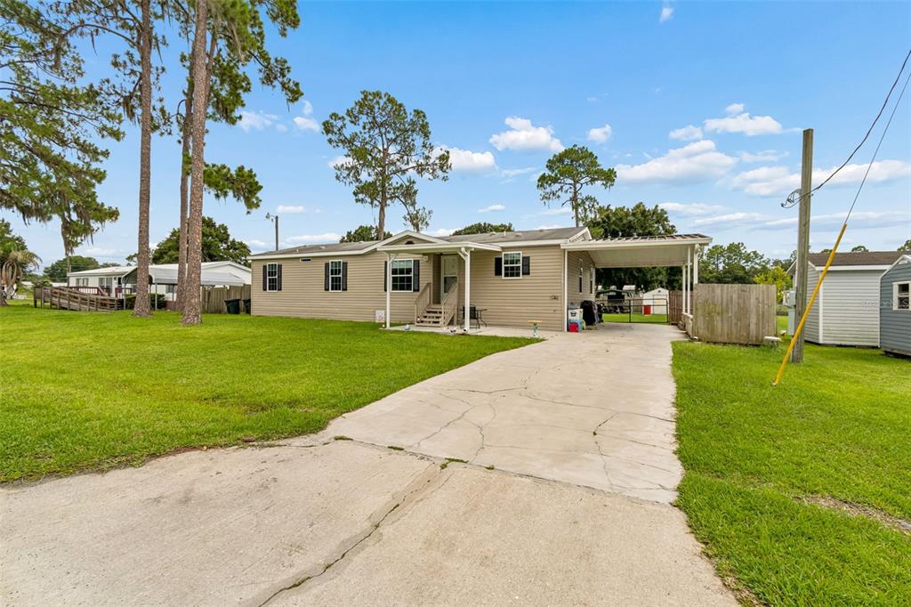 A single-story manufactured home with a concrete driveway, carport, and a large grassy yard — 4917 HERNDON WAY, AUBURNDALE, FL