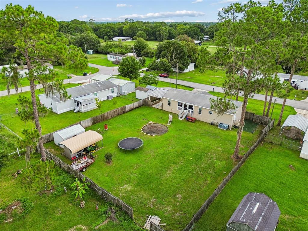 An aerial view shows a fenced backyard with a trampoline, shed, and carport behind houses — 4917 HERNDON WAY, AUBURNDALE, FL