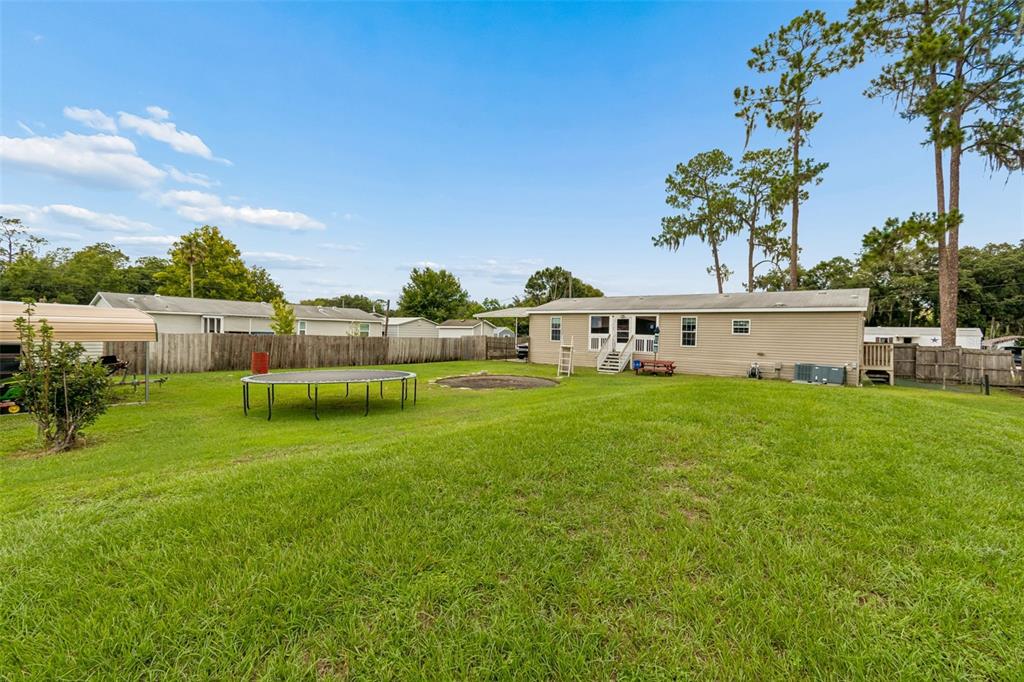 A grassy backyard features a trampoline, a fire pit, and a single-story house with siding — 4917 HERNDON WAY, AUBURNDALE, FL