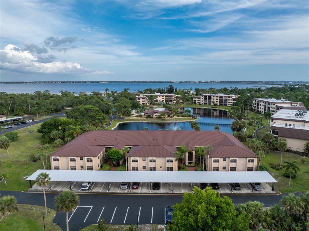 An aerial view shows a multi-story apartment building with a covered parking area and pond — 23465 HARBORVIEW ROAD UNIT 1026, PUNTA GORDA, FL