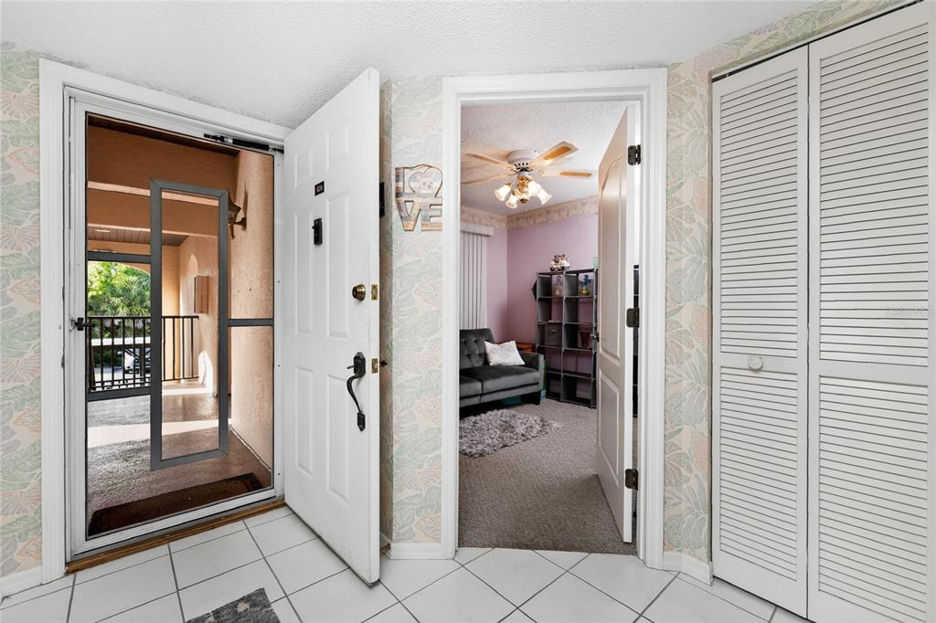 An entryway with white tile floors, a front door, and a doorway leading to a bedroom — 23465 HARBORVIEW ROAD UNIT 1026, PUNTA GORDA, FL