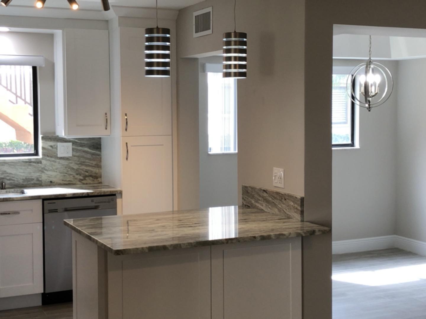 A kitchen with white cabinets, stone countertops, and pendant lights, viewed from a dining area — 15090 Ashland Place, Delray Beach FL 33484, DELRAY BEACH, FL
