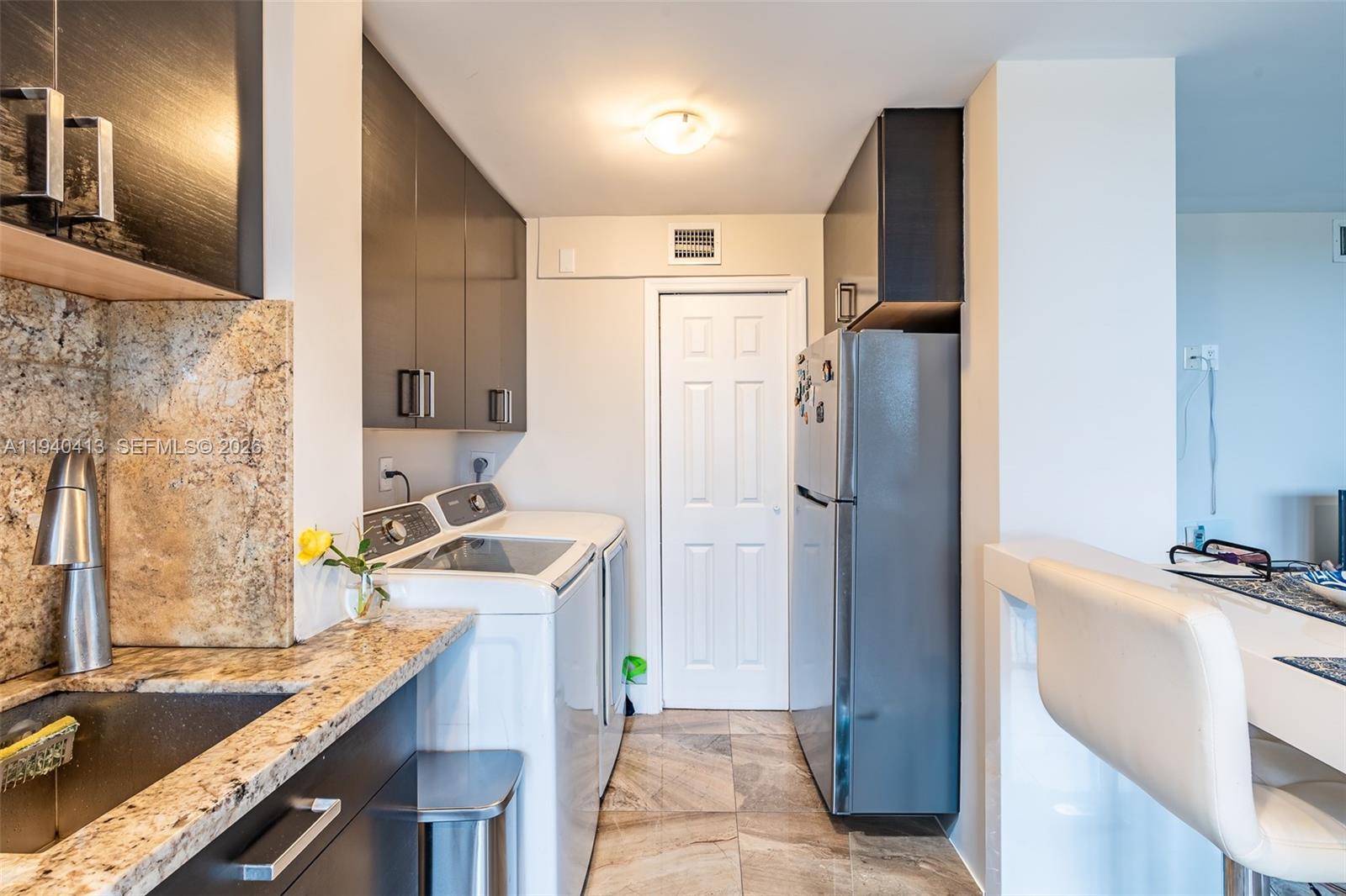 A kitchen features dark cabinets, granite countertops, stainless steel appliances, and an integrated laundry area — 3400 Blue Lake Dr # 505, Pompano Beach FL 33064, POMPANO BEACH, FL