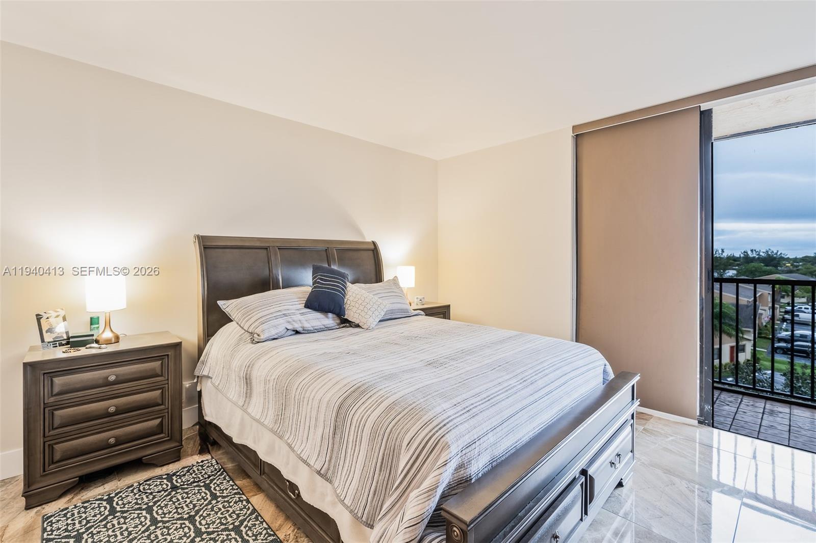 A bedroom features a dark wood bed, a matching nightstand, and a balcony with views — 3400 Blue Lake Dr # 505, Pompano Beach FL 33064, POMPANO BEACH, FL