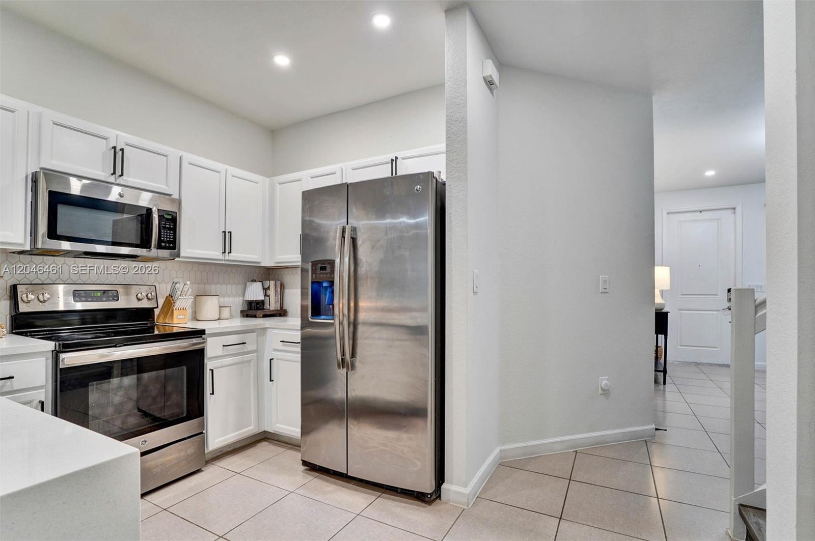 A kitchen features white cabinets, stainless steel appliances, and light-colored tile flooring — 25341 SW 115th Ct, Homestead FL 33032, HOMESTEAD, FL
