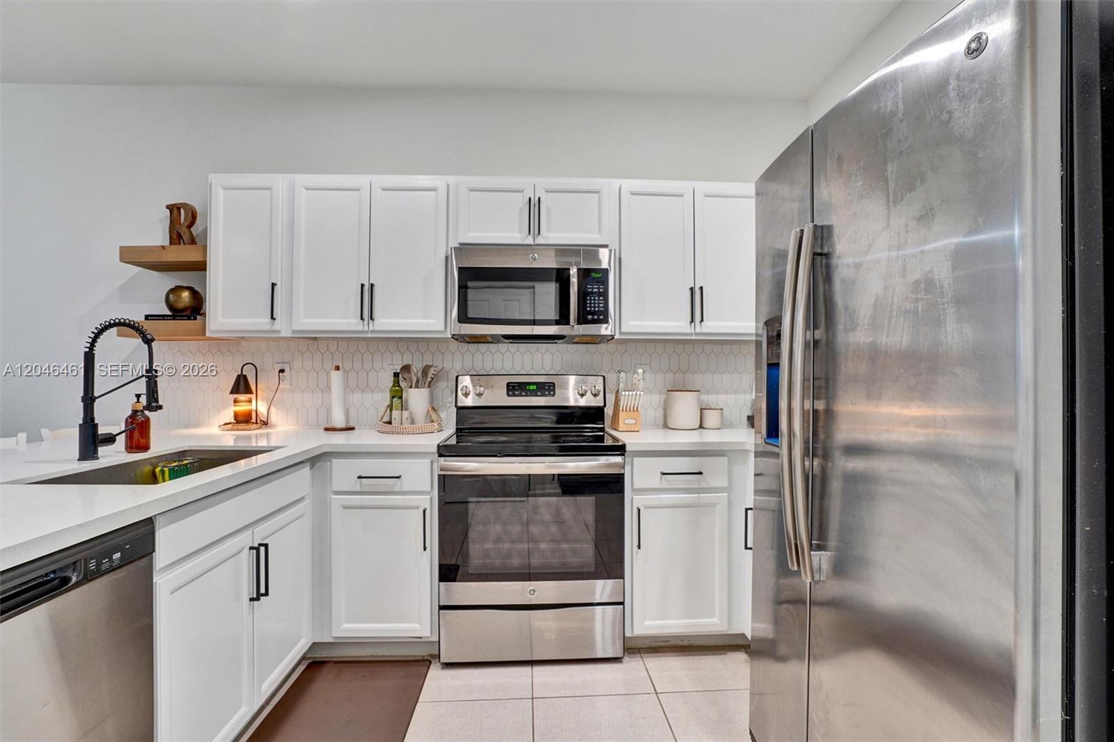 A kitchen features white cabinets, stainless steel appliances, a tiled backsplash, and light countertops — 25341 SW 115th Ct, Homestead FL 33032, HOMESTEAD, FL
