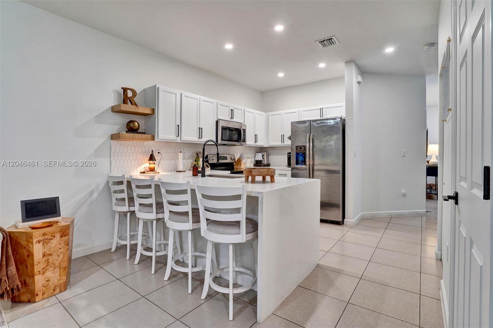 A modern kitchen features white cabinets, stainless steel appliances, and a waterfall island with seating — 25341 SW 115th Ct, Homestead FL 33032, HOMESTEAD, FL