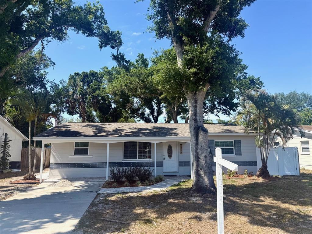 A single-story house with light siding, a covered front porch, and mature trees in front — 5731 66TH AVENUE N, PINELLAS PARK, FL