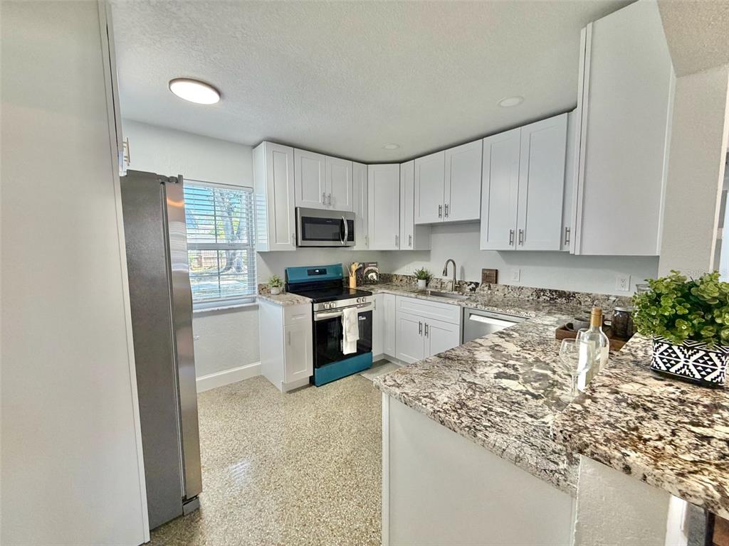 A kitchen features white cabinets, granite countertops, stainless steel appliances, and speckled flooring — 5731 66TH AVENUE N, PINELLAS PARK, FL