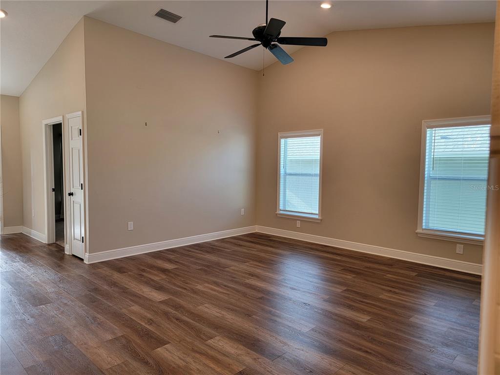 An empty room features vaulted ceilings, a ceiling fan, two windows, and wood-look flooring — 5986 TEAL TRAIL, LAKELAND, FL