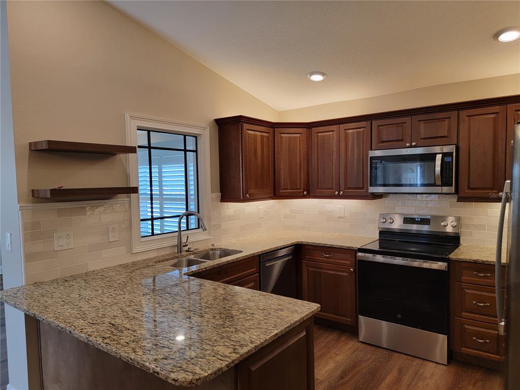A kitchen features dark wood cabinets, granite countertops, stainless steel appliances, and a tiled backsplash — 5986 TEAL TRAIL, LAKELAND, FL
