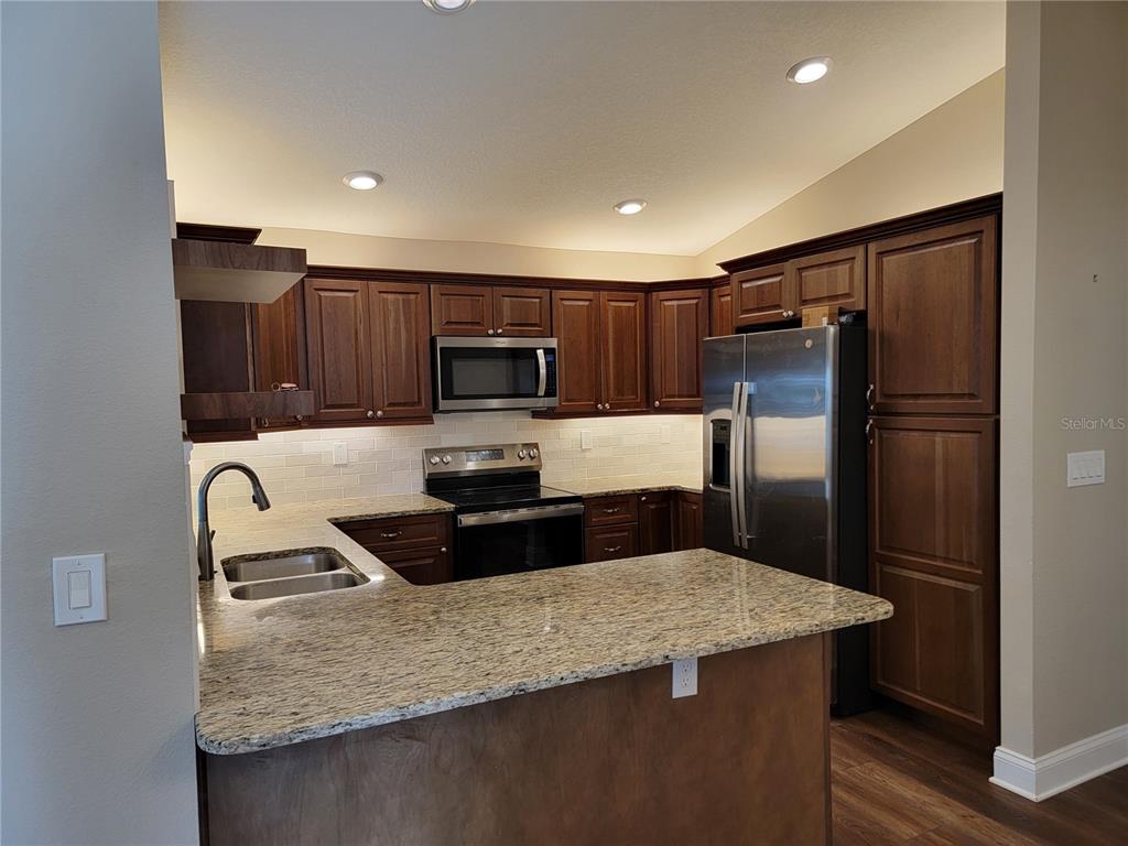 A kitchen features dark wood cabinets, granite countertops, stainless steel appliances, and a peninsula — 5986 TEAL TRAIL, LAKELAND, FL